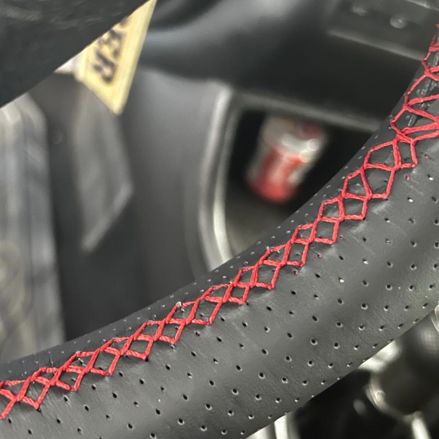 Volante forrado en piel negra con costura roja en un coche atendido en el taller